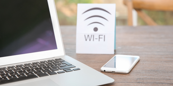Imagem de um notebook com celular e a placa de que há Wi-fi no local.